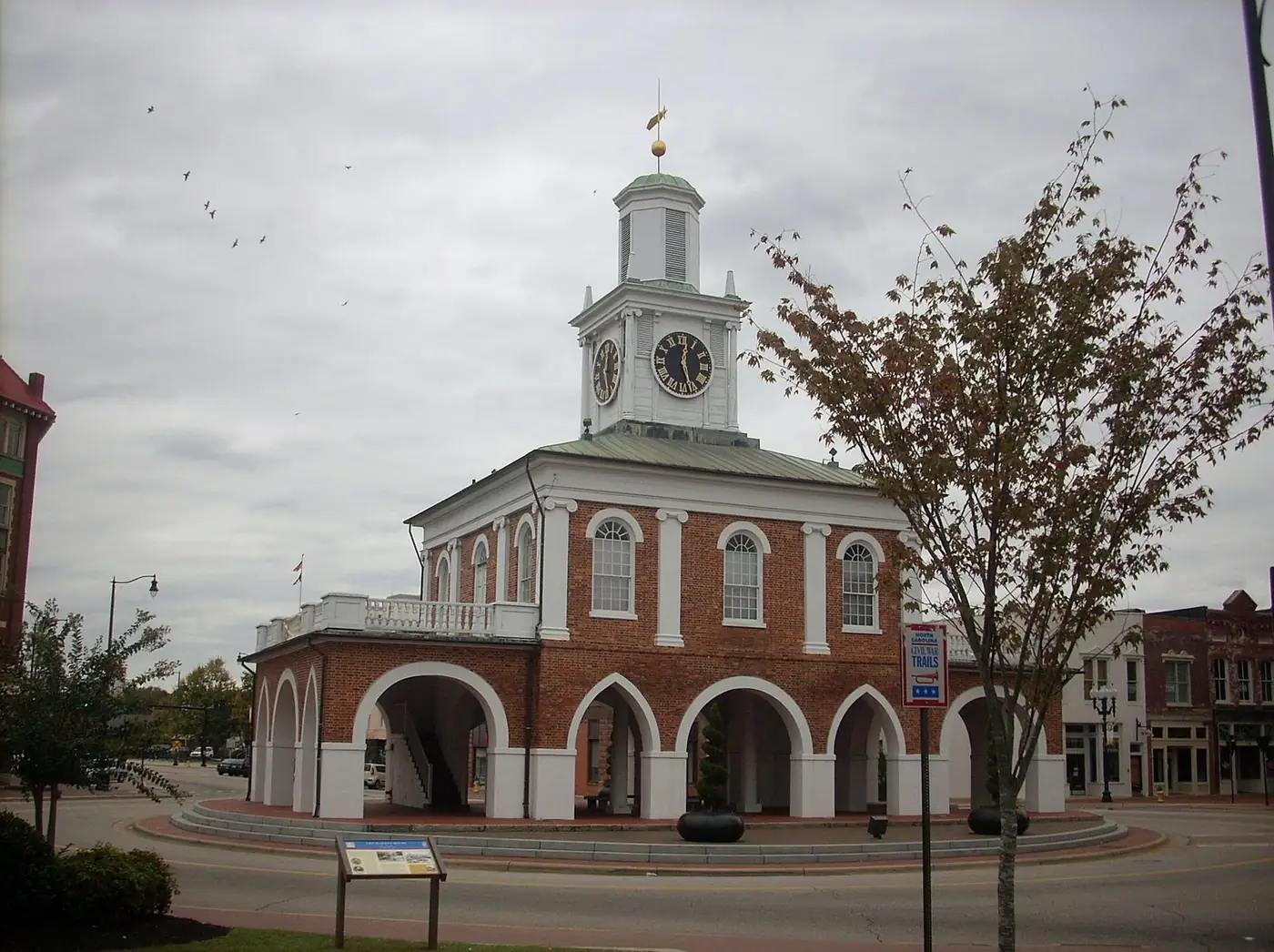Brick Market House with white arches and a clock cupola at the center of a downtown traffic circle